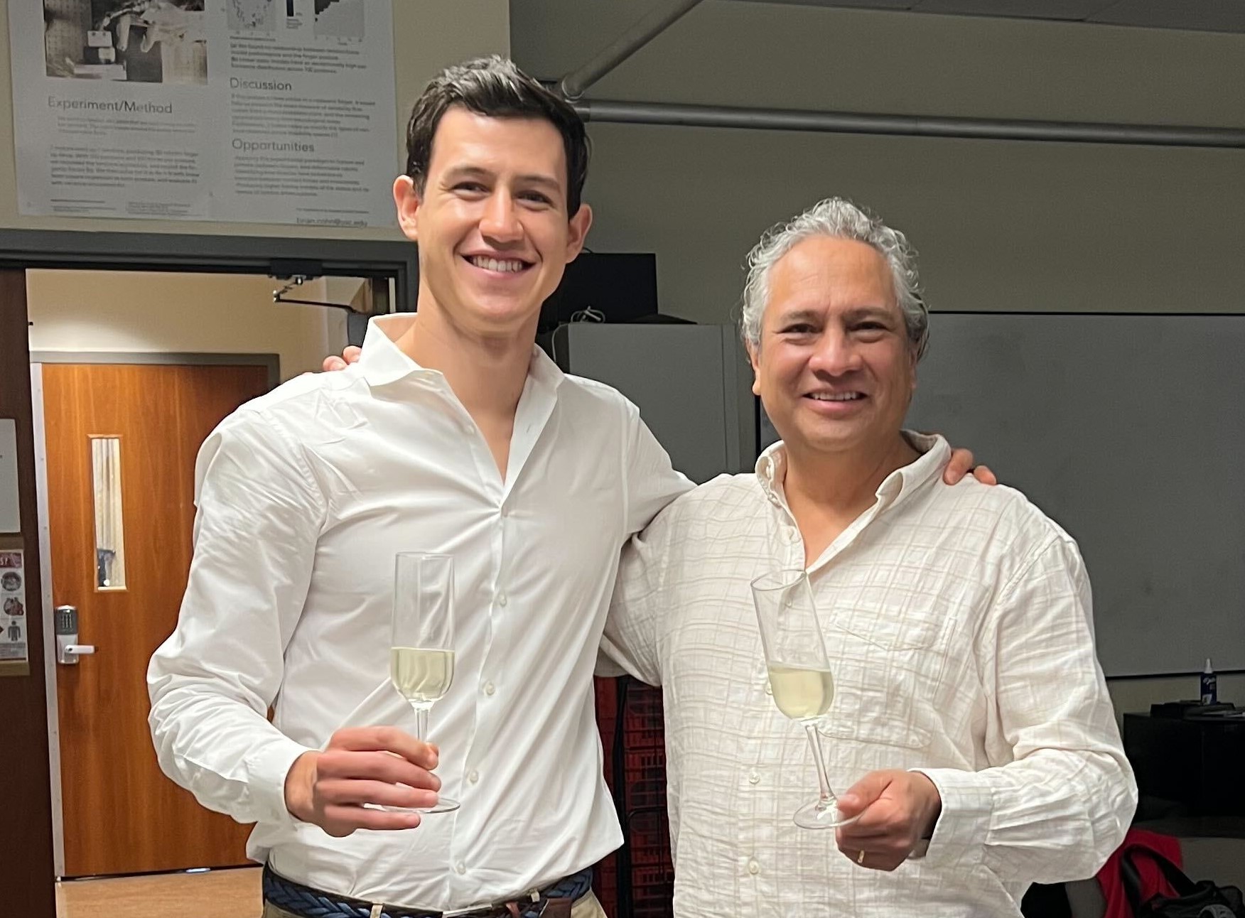 Darío Urbina-Meléndez (left) and Francisco Valero-Cuevas (right) toast with champagne while smiling at the camera.